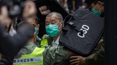 Miljonären Jimmy Lai eskorteras från häktet till domstol under hård polisbevakning.