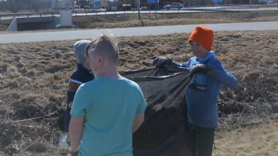 Tre barn plockar skräp i en stor sopsäck