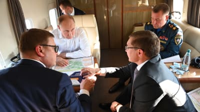 Vladimir Putin sitter i ett privatplan med katastrofminister Jevgeni Zinitjev och andra ministrar.