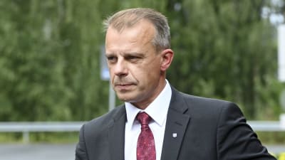 Centerns gruppordförande Juha Pylväs iklädd kostym och vinröd slips. i bakgrunden gröna lummiga träd.