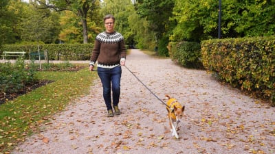 En kvinna är ute och går med sin hund i en park.