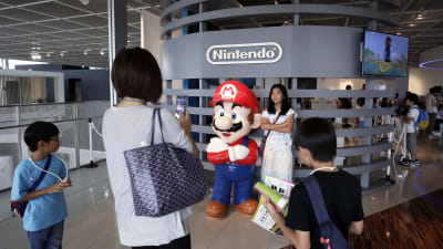 Henkilö asettautuu valokuvattavaksi Super Mariota esittävän mainosnuken viereen.