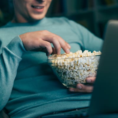Man tittar på film på laptop och äter popcorn