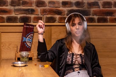 En kvinna med hörlurar sitter vid ett bord och röker en joint