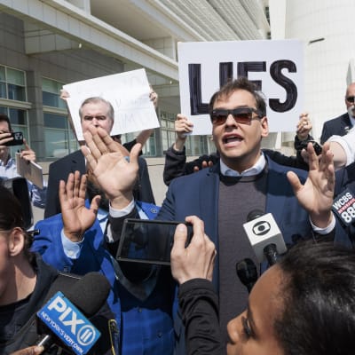 George Santos omgiven av journalister. Bakom honom håller någon upp en skylt med ordet "Lies" (lögner).