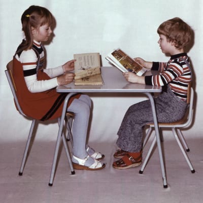 Dagisbild från sjuttiotalet. En flicka och pojke sitter mittemot varandra och läser i profilbild.