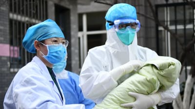 Sjukhuspersonal i Xi'an, i nordvästra Kina, visar up en flickbaby som föddes i lördags. Mamman var smittad av coronaviruset, men flickan är frisk. Relativt få barn har insjuknat i covid-19 och dödligheten i viruset stiger med åldern. 