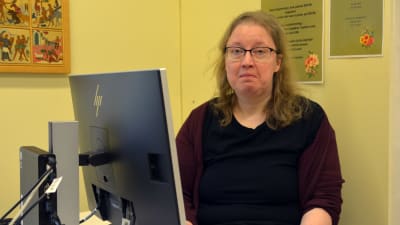 En kvinna sitter framför en dator. Hon tittar in i kameran.