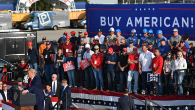 Donald Traump på massmöte utomhus, banderoll om att köpa amerikanskt