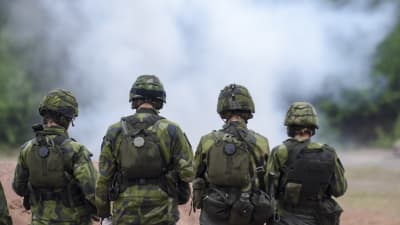 Soldater i stridsmundering står framför rök. De svenska soldater deltar i ett slutprov 2014.