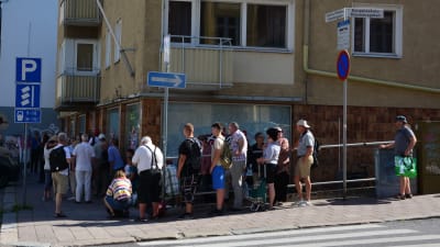 Ett femtiotal personer står i kö längs trottoaren.