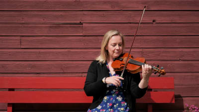 Gabriella Nikula spelar fiol på en bänk i Kaustby.