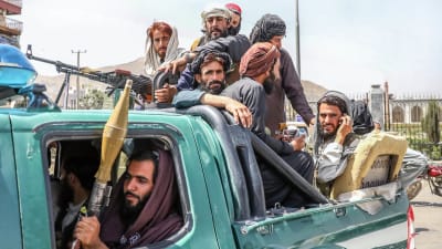 Talibanern med vapen och telefoner i händerna sitter på ett flak.