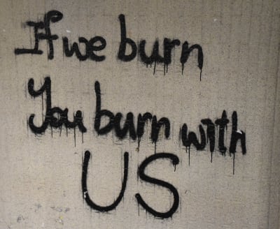 Betongvägg med graffititexten ''If we burn, you burn with us''.