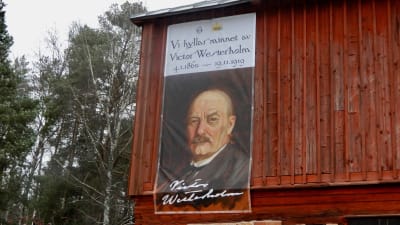 En väggboning föreställande en man med mustasch. Väggboningen är uppsatt på sidan av ett rött hus.