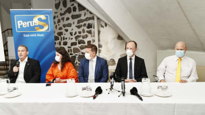 Män och kvinnor sitter bakom ett bord. Alla bär munskydd utom en man längst till vänster. Sannfinländska politiker i Åbo 26.8.2020.