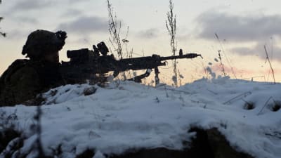 En soldat ligger i snön siktandes med sitt vapen.