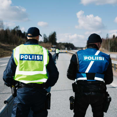 Två poliser i uniform fotograferade bakifrån medan de står på en väg.