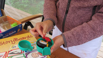 Undervisningsmaterial som används i talterapi för barn, plastleksaker. Kvinnohänder håller i en pingvin och en fisk i en grön igloo plus kort som föreställer saker såsom paraply, tåg, sol och elefant.