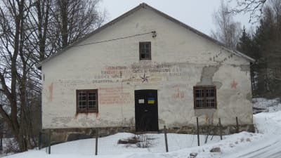 En gammal vit tegelbyggnad. På fasaden gammal rysk text (från Porkala-parentesen). På dörren en nutida gul- och båtejpad ruta som symboliserar den ukrainska flaggan.