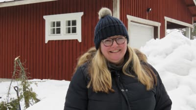 Pauliina Sjöholm ute i Sjundeå i vitt vinterlandskap. Bakom ett rött trähus.
