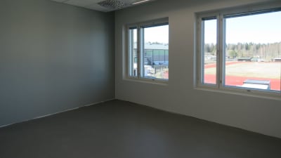 Ett rum med stora fönster med utsikt öer Sjundeås sportplan och löpbanor. Väggarna i ljusgrått. Personalrum för läare eller rektorer.