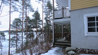 Ett gult trähus med både balkong och altan som vetter mot havet. Vinter, snö och is.