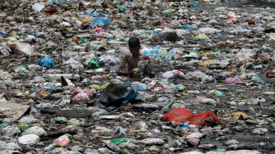 En pojke i New Delhi står med avfall upp till midjan och söker efter saker som kan återanvändas. 