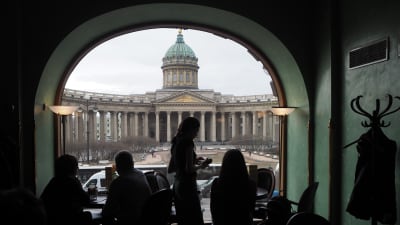Vy från ett café i S:t Petersburg. I förgrunden syns människor som står framför ett bågformat fönster i motljus.