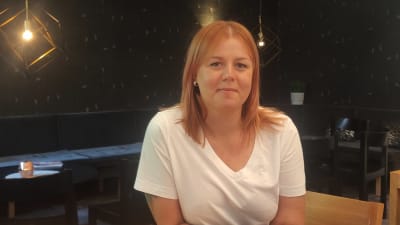 Porträtt på Ida-Maria Pekkarinen iklädd en vit t-skjorta mot en mörk bakgrund.