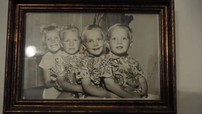 fyra ljushåriga glada barn sitter i kö med armarna runt varandra på svartvitt fotografi i ram