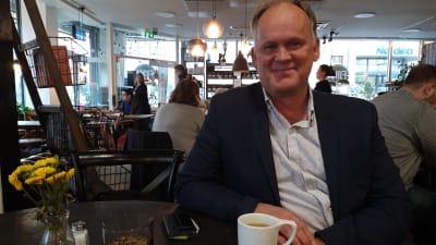 Owe Sjölund sitter på ett kafé med en kopp kaffe. 