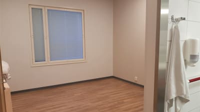Ett rum med ljust golv och vita vägger. Toaletten skymtar till höger,