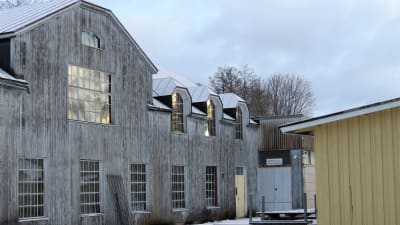 En stor byggnad i grått trävirke med stora fönster men med små fönsterrutor. Finns i Billnäs och kallas Övre snickeriet eller Ylä-Nikkari. Vinter och snö.