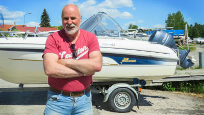 En man står framför sin båt som han har på en båttrailer. Trailern är fast i en större personbil. Sommar och soligt. Mannen har armarna i kors framför bröstet och ser nöjd ut.