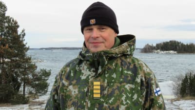 Portättbild på brigadkommendör, kommodor Juha Kilpi, Nylands brigad. Han står ute i Syndalen, vinter. Bakom hav och man kan skymta några Jurmobåtar, öppet vatten.