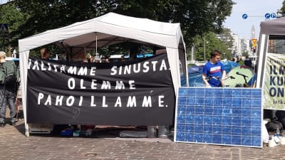 Ett tält med en stor skyld där det står "Vi ber om ursäkt för att vi bryr oss om dig" på finska.