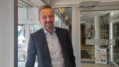 Man lutar sig mot ett fönster och ler mot kameran.