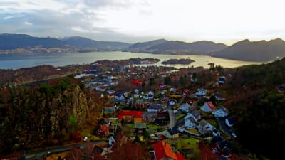 Flygbild över samhälle med havsvik och fjäll i bakgrunden.
