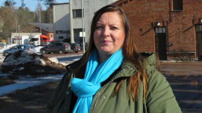 Profilbild på Piia Hasselberg, hon står utomhus, mars 2022, bakom röd tegelbyggnad på gamla Ekåsenområdet.