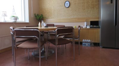 Ett runt bord med stolar i ett litet kontor tänkt för distansarbete. Gröna växter vid fönstret och en klocka på väggen.