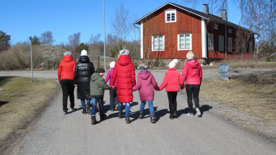 En grupp med barn och några vuxna på promenad i Hangö. Sol och vår. Man ser bara ryggarna.