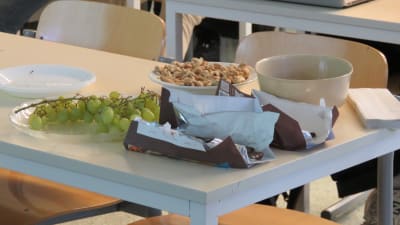 Vindruvor, choklad och nötter i skålar på ett bord i ett klassrum i en skola.