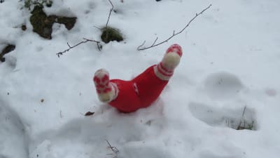 Tygdocka i snön. Man ser bara  röda byxor och yllesockor i vitt med röda hjärtan. Ska föreställa en tomtesom sprattlar i snön, med huvudet täckt av snö. Julstigen i Hangö 2022.
