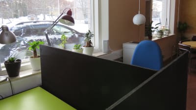 Ett litet kontor för distansjobb. Kontorsstol, arbetsbord, en printer i bakgrunden. Fönster med snölandskap ute.