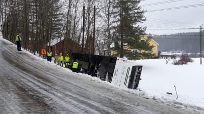 En buss ligger på sidan i diket, räddningsmanskap jobbar