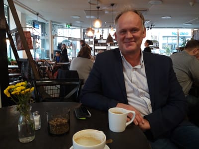 Owe Sjölund sitter på ett kafé med en kopp kaffe. 