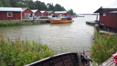 Fagerö i Pyttis, vy ut över havet. Flera röda träbodar vid stranden och en båt vid en brygga.