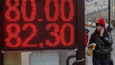 En kvinna passerar en skylt med rubelns valutakurs.
