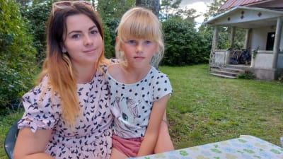 Två systrar. Den sjuåriga sitter i den nittonårigas famn framför det hus de numera bor i på Gotland efter att de har flytt med resten av familjen från Gammalsvenskby i Ukraina 